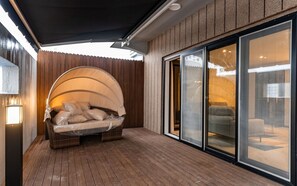 Un área de patio techada con un conjunto de asientos acolchados, una terraza de madera y un ventanal corredero que da a un espacio interior.