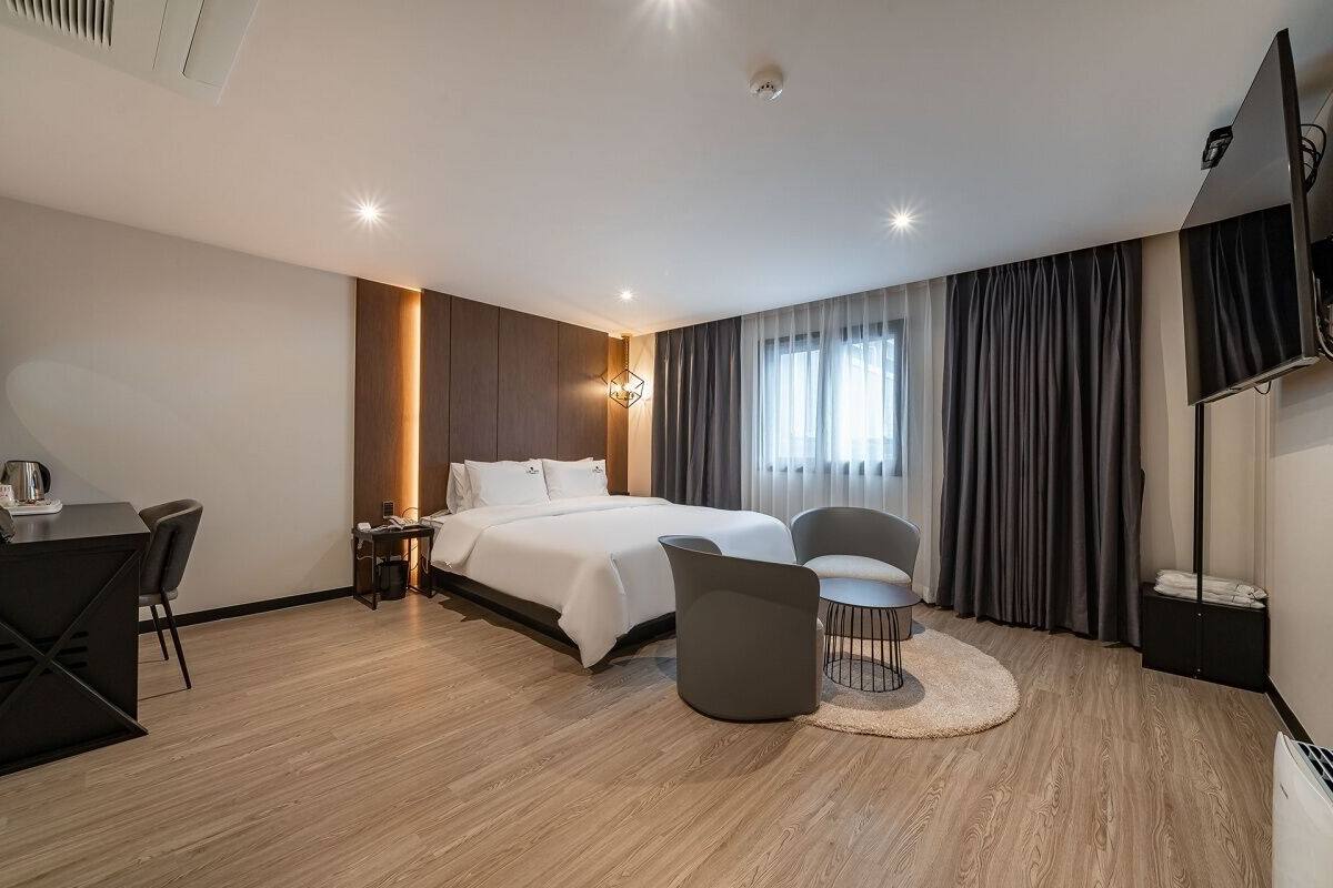 A modern hotel room with a bed, a desk, a chair, a TV, and a large window with curtains.