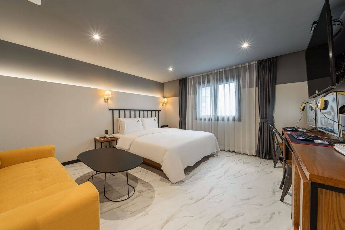 A hotel room with a bed, a desk with a computer, a chair, and a sofa.