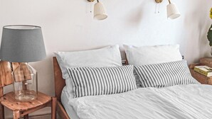 A bed with white bedding, a striped pillow, a wooden nightstand with a lamp, and two wall-mounted light fixtures.