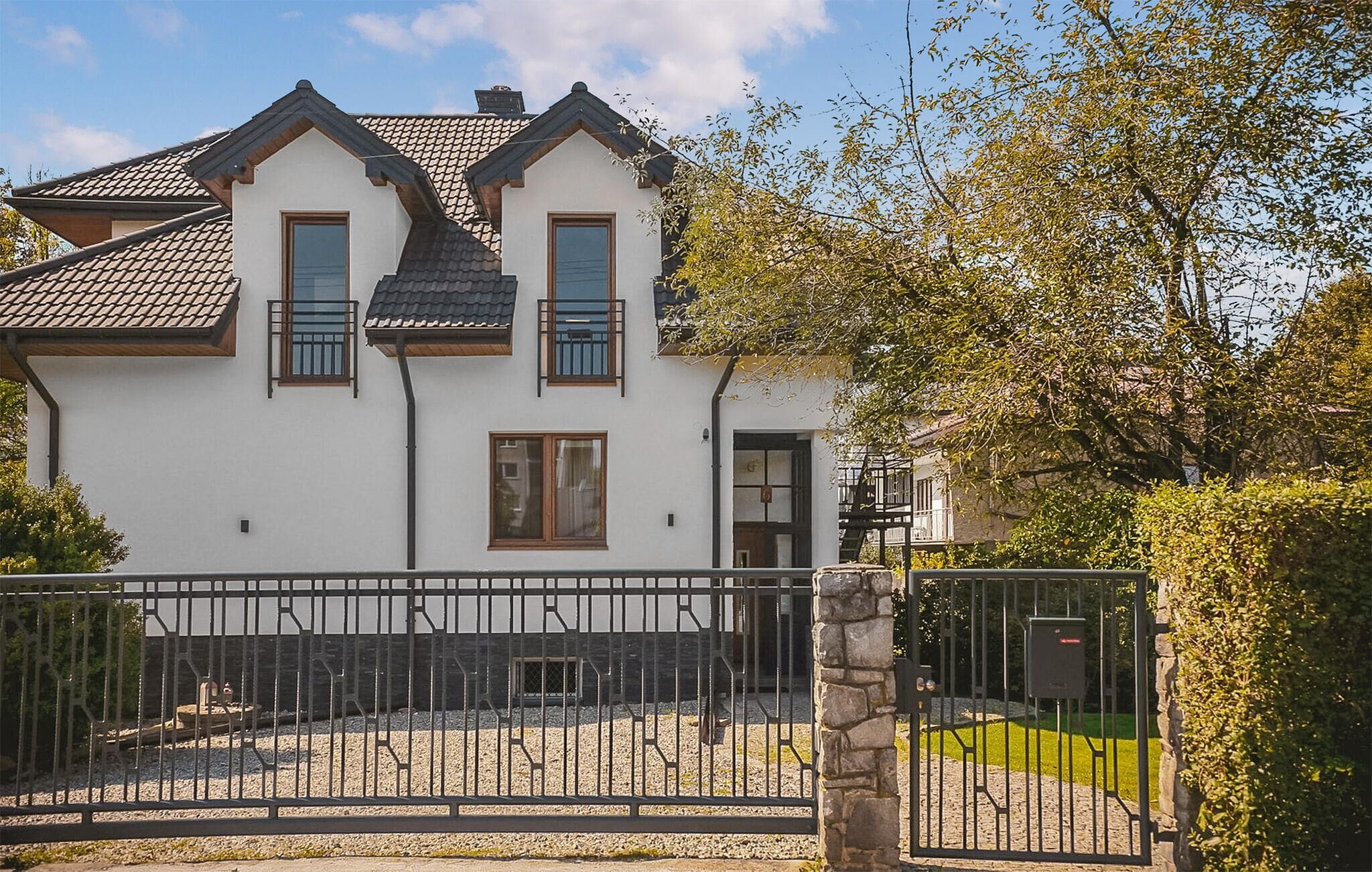 A two-story house with a white exterior, a tiled roof, and a gated driveway.