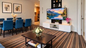 A modern living room with a dining area, a flat-screen TV, and a bookshelf.