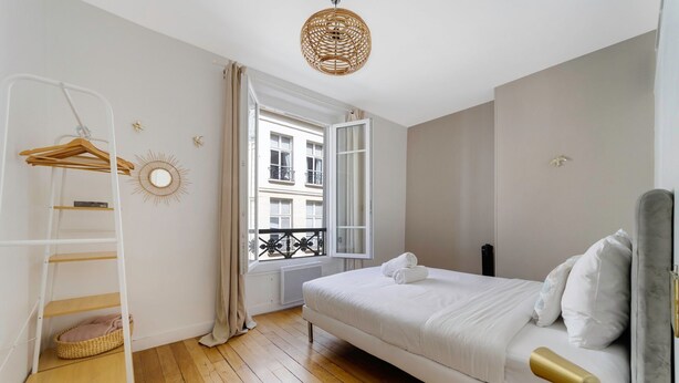 A bedroom with a bed, a hanging light fixture, a window with curtains, a radiator, and a wooden floor. - So Chic Montorgueil Paris (Paris)
