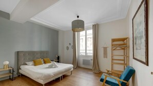Een slaapkamer met een bed, nachtkastje, lamp en stoel.