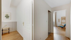 Een gang met een witte deur, een ingelijst schilderij aan de muur en een blauwe stoel op de achtergrond.