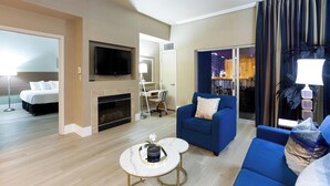 A hotel room with a bed, a TV, a fireplace, a blue sofa, a coffee table, and a view of a cityscape through the window.
