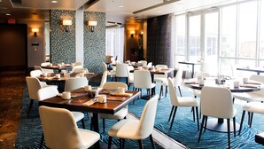 A hotel dining area with multiple tables and chairs, large windows, and decorative wall tiles.