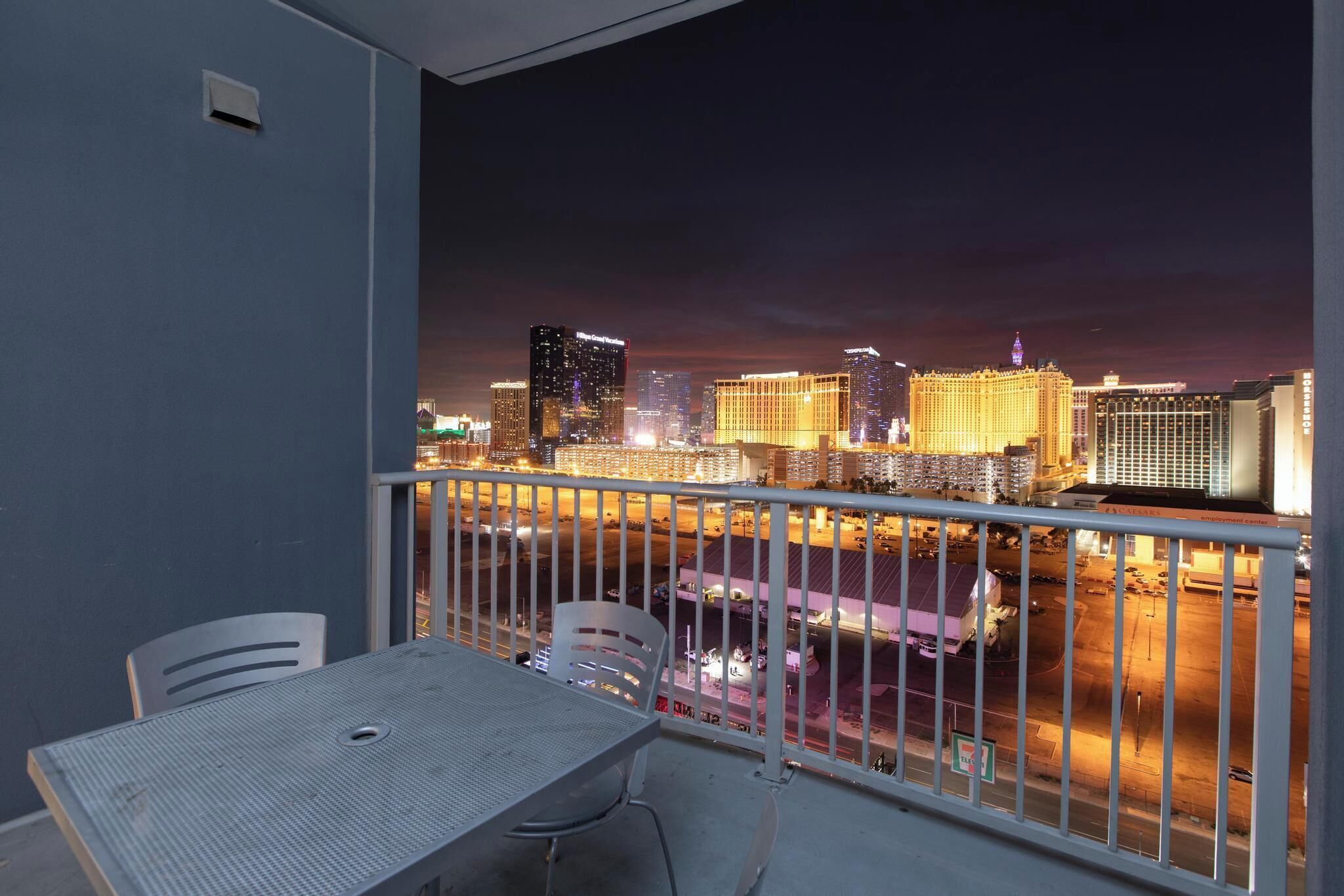 Un balcone con tavolo e sedie, vista sulla città illuminata di notte.