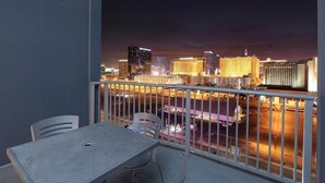 A balcony with a table and chairs, overlooking a cityscape at night.