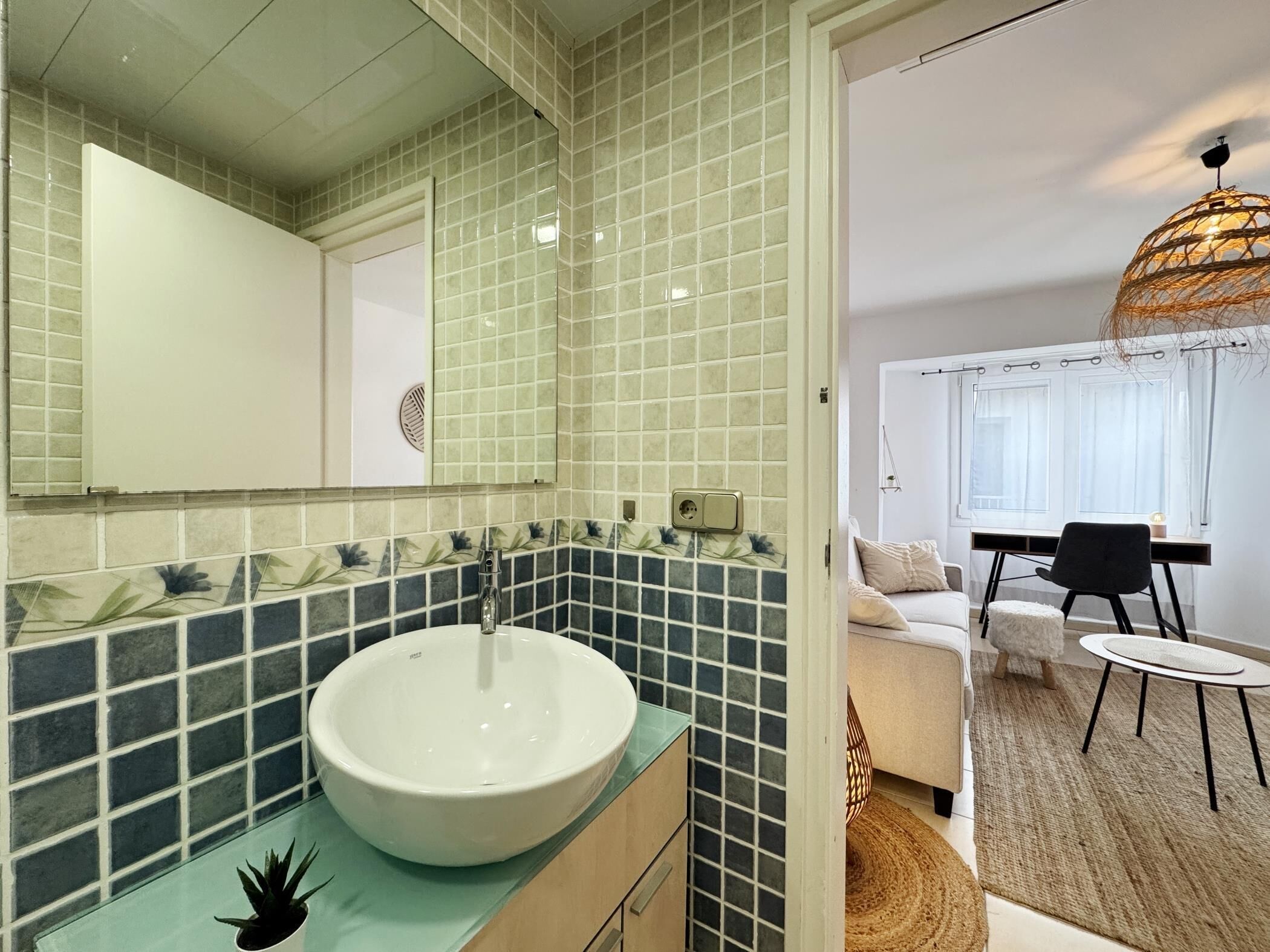 Une salle de bain avec un lavabo blanc, des carreaux verts et bleus, et un miroir.