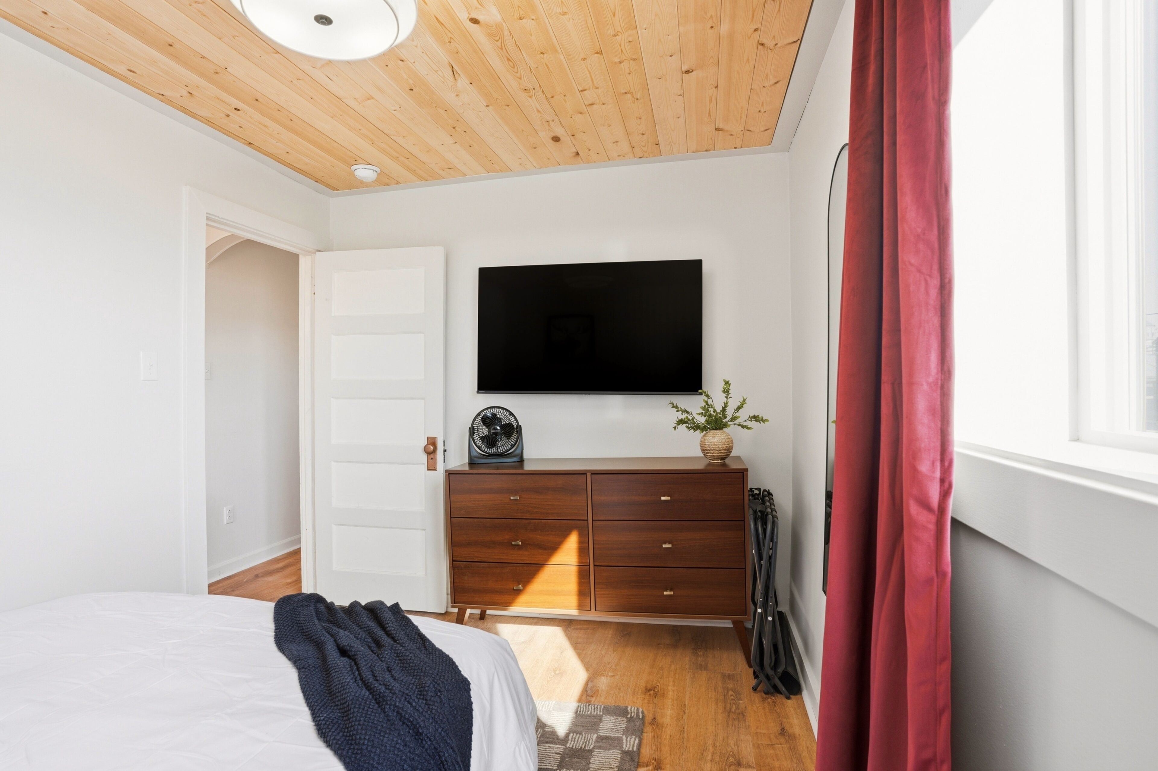 A bedroom with a bed, a dresser, a television, and a window with curtains.