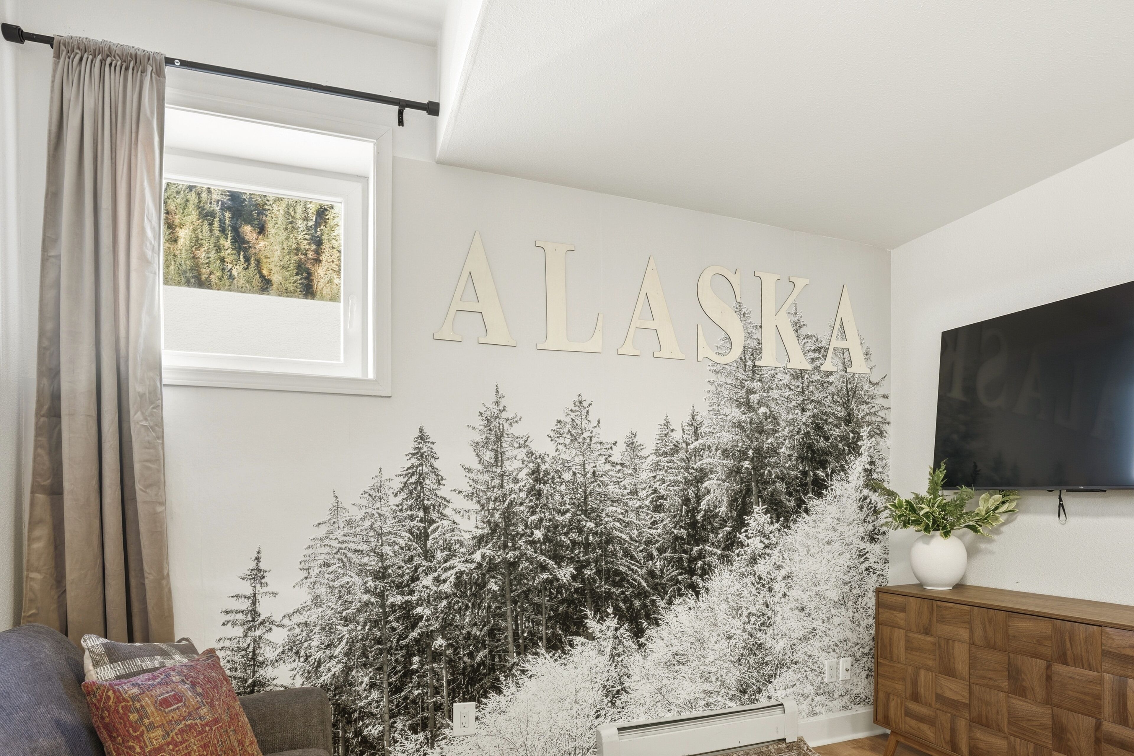 Uma sala de estar com um grande letreiro 'ALASKA', uma TV e uma lareira.
