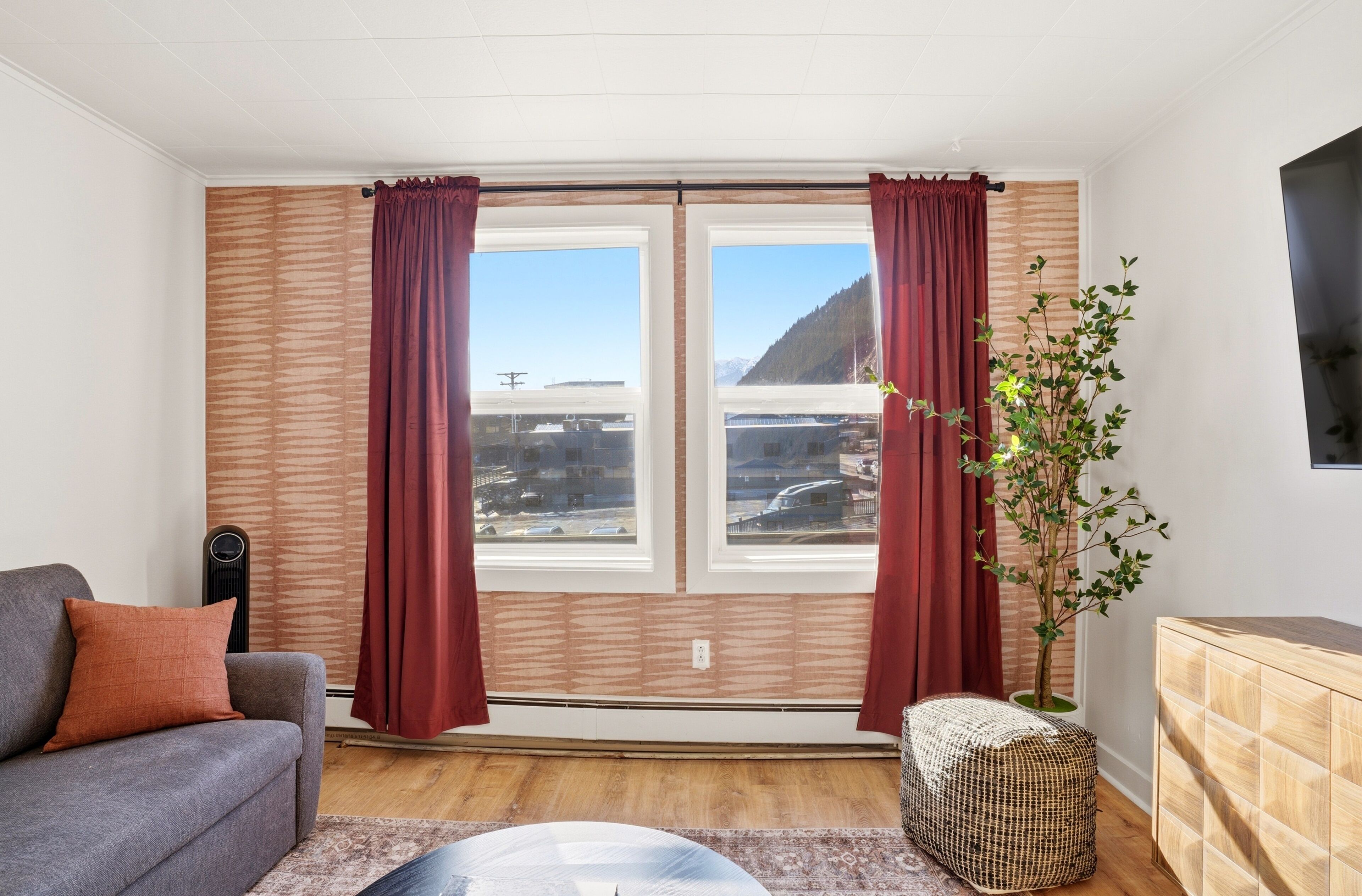 A room with a sofa, a small table, a plant, and a window with curtains.