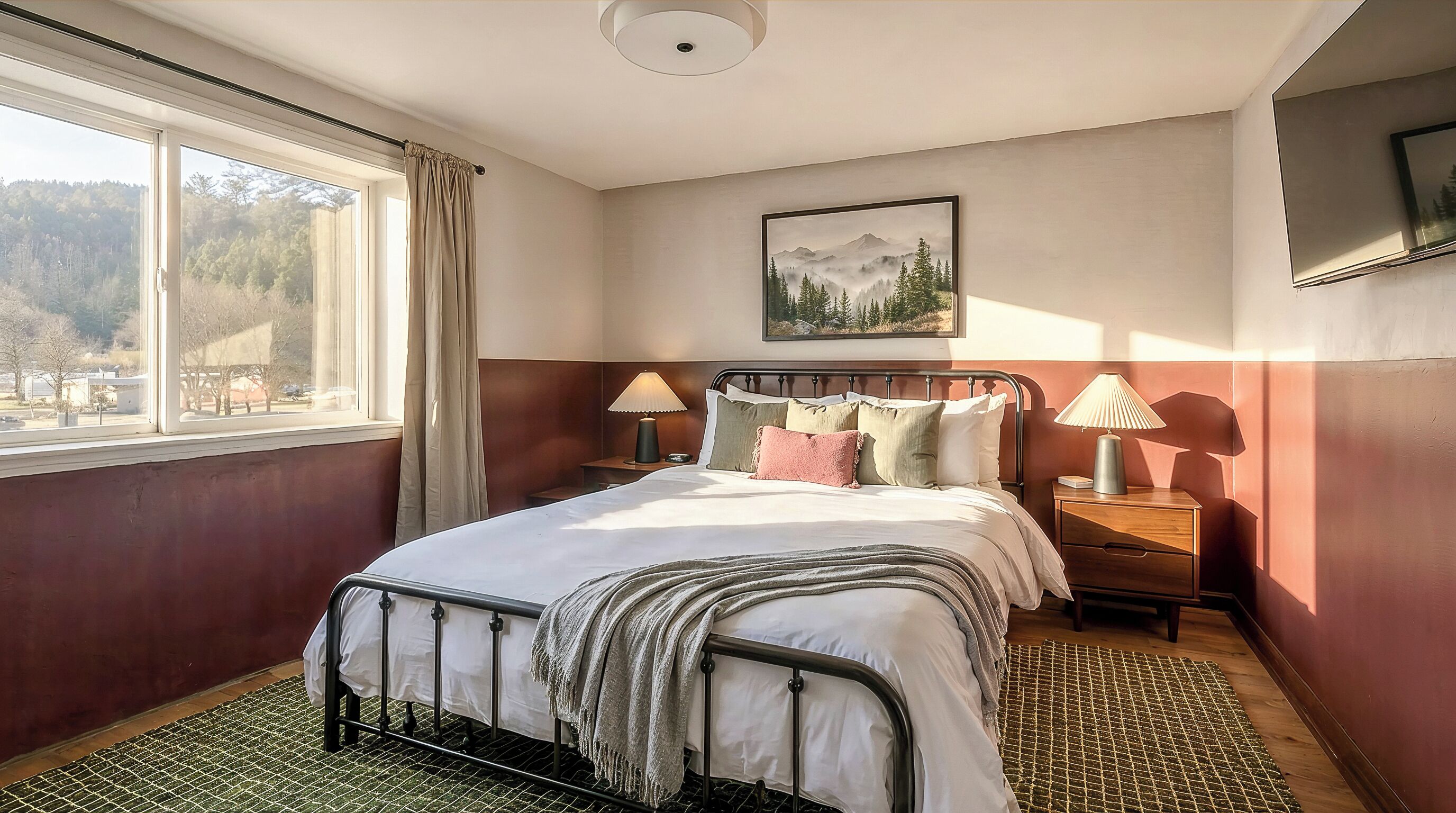 Quarto com cama, duas mesas de cabeceira, janela com cortinas, um quadro na parede e vista para árvores lá fora.