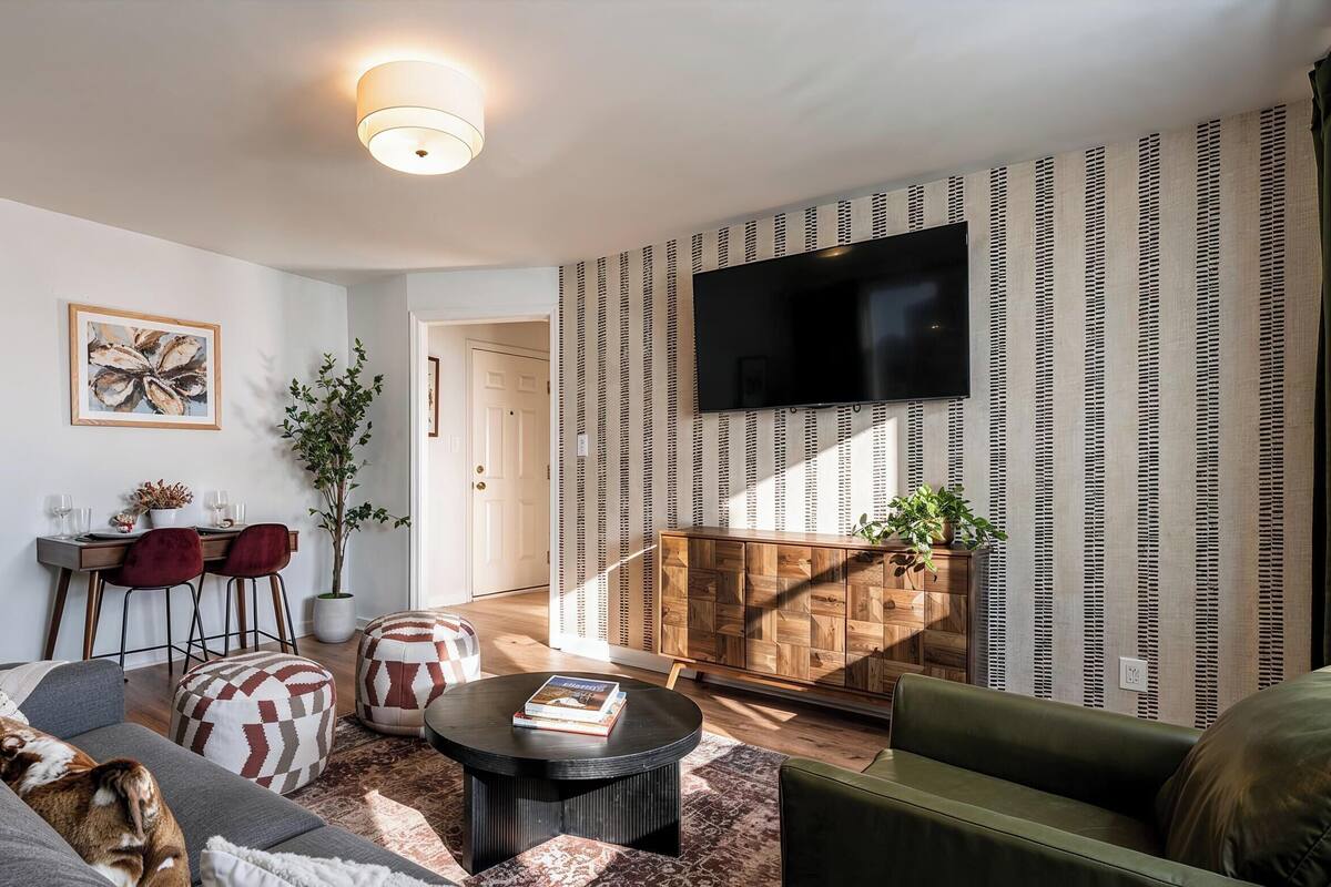 Ein Wohnzimmer mit Sofa, Poufs, Couchtisch, Fernseher und Wand mit Muster.