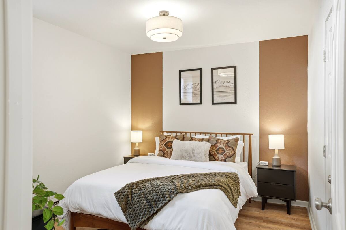 Ein Schlafzimmer mit Bett, Nachttischen, Wandbildern und einer Pflanze.