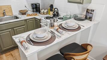 A kitchen with a marble countertop, green cabinets, a coffee maker, a kettle, and a dining area with a table set for two.