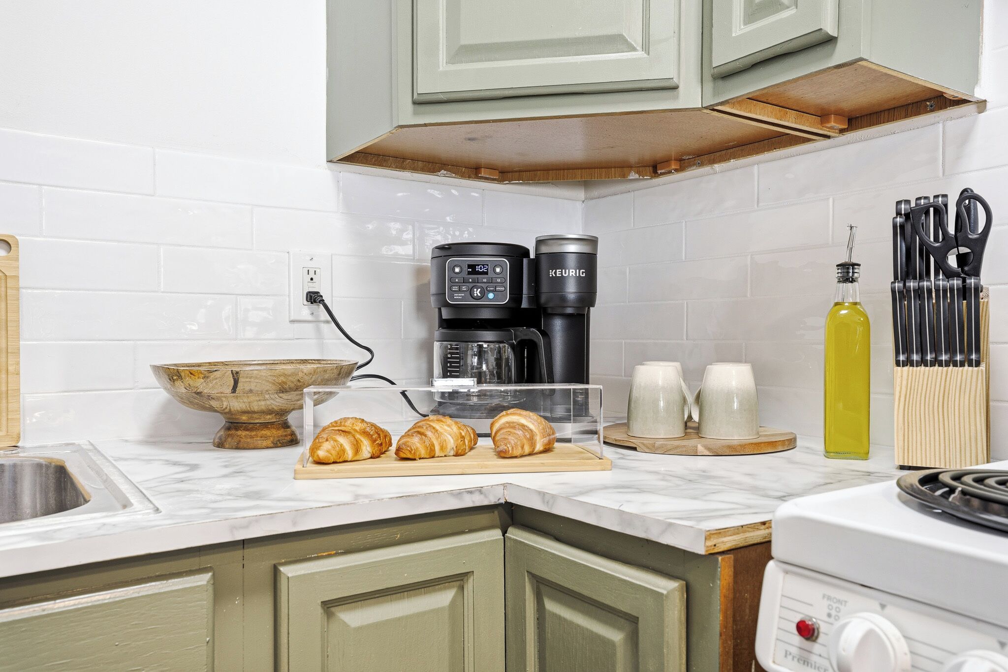 A kitchen with a coffee maker, a microwave, a kettle, a sink, and a stove.