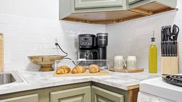 A kitchen with a coffee maker, a microwave, a kettle, a sink, and a stove.