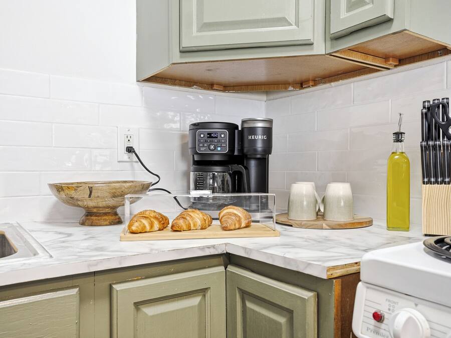 A kitchen with a coffee maker, a microwave, a kettle, a sink, and a stove.