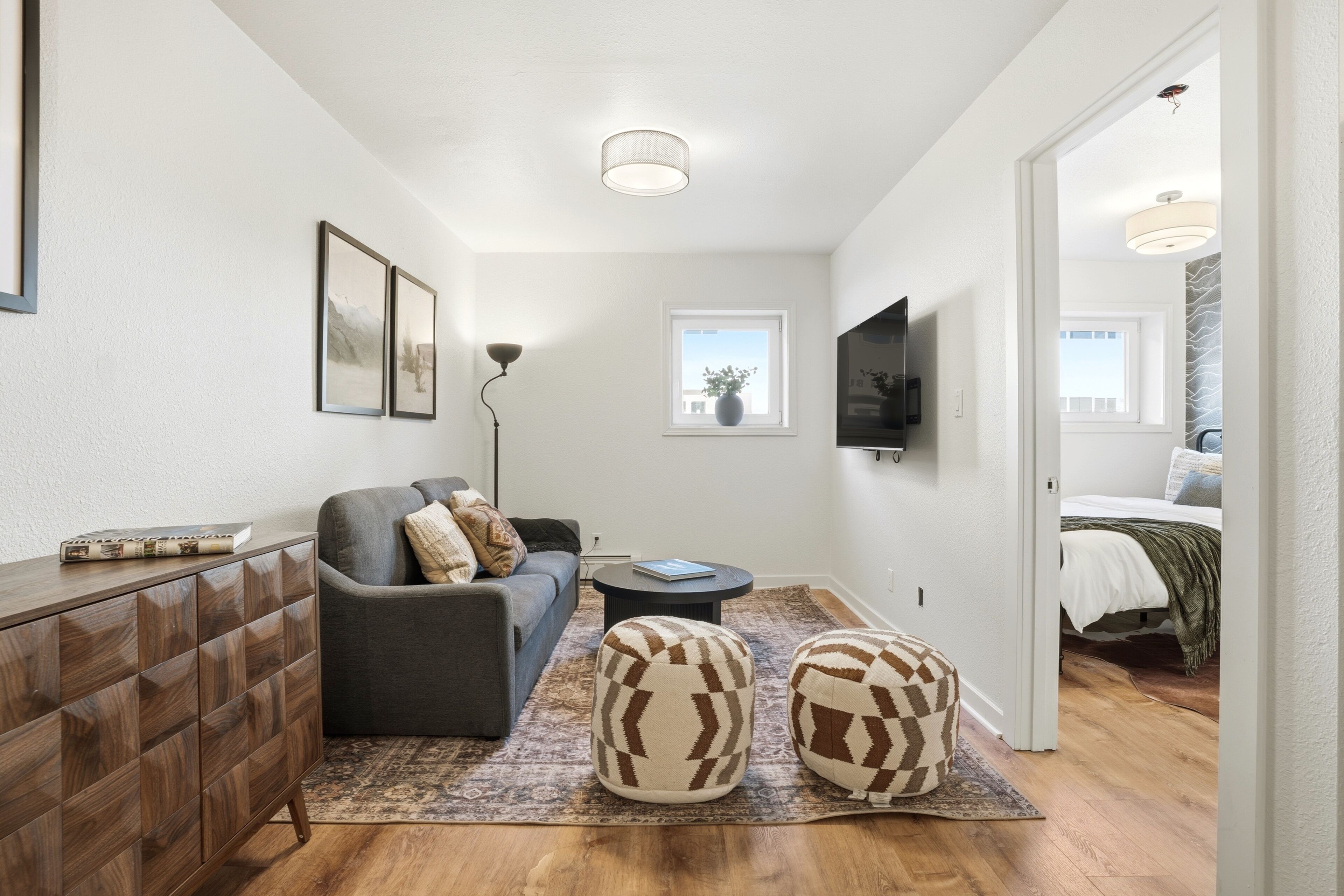 A modern living room with a sofa, ottomans, a coffee table, and a TV mounted on the wall.
