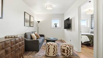 A modern living room with a sofa, ottomans, a coffee table, and a TV mounted on the wall.