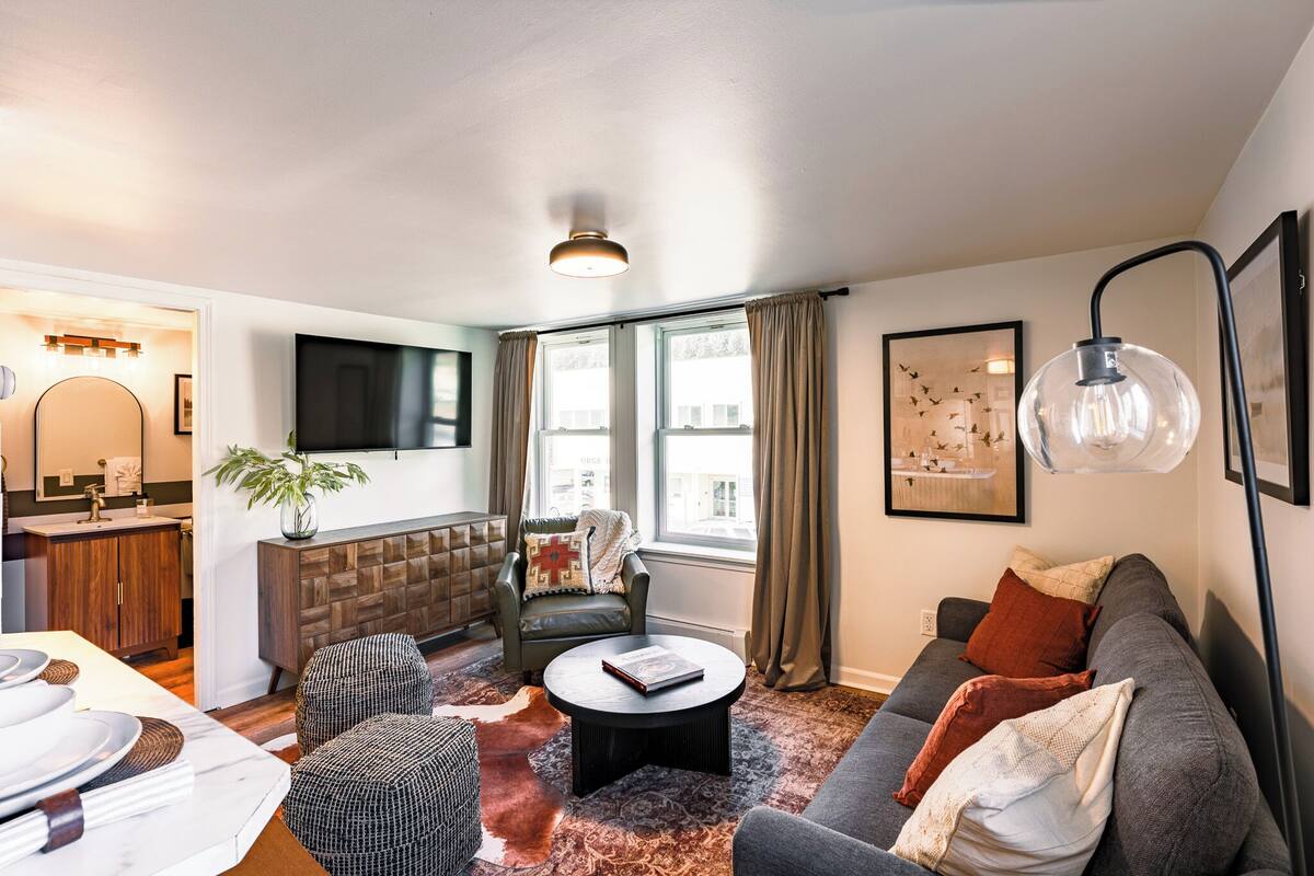 Ein Wohnzimmer mit Sofa, Sessel, Couchtisch und einem an der Wand befestigten Fernseher.