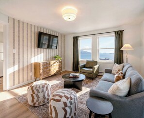 Una sala de estar con sofá, sillón, reposapiés, mesa de centro, televisor y vistas al mar.