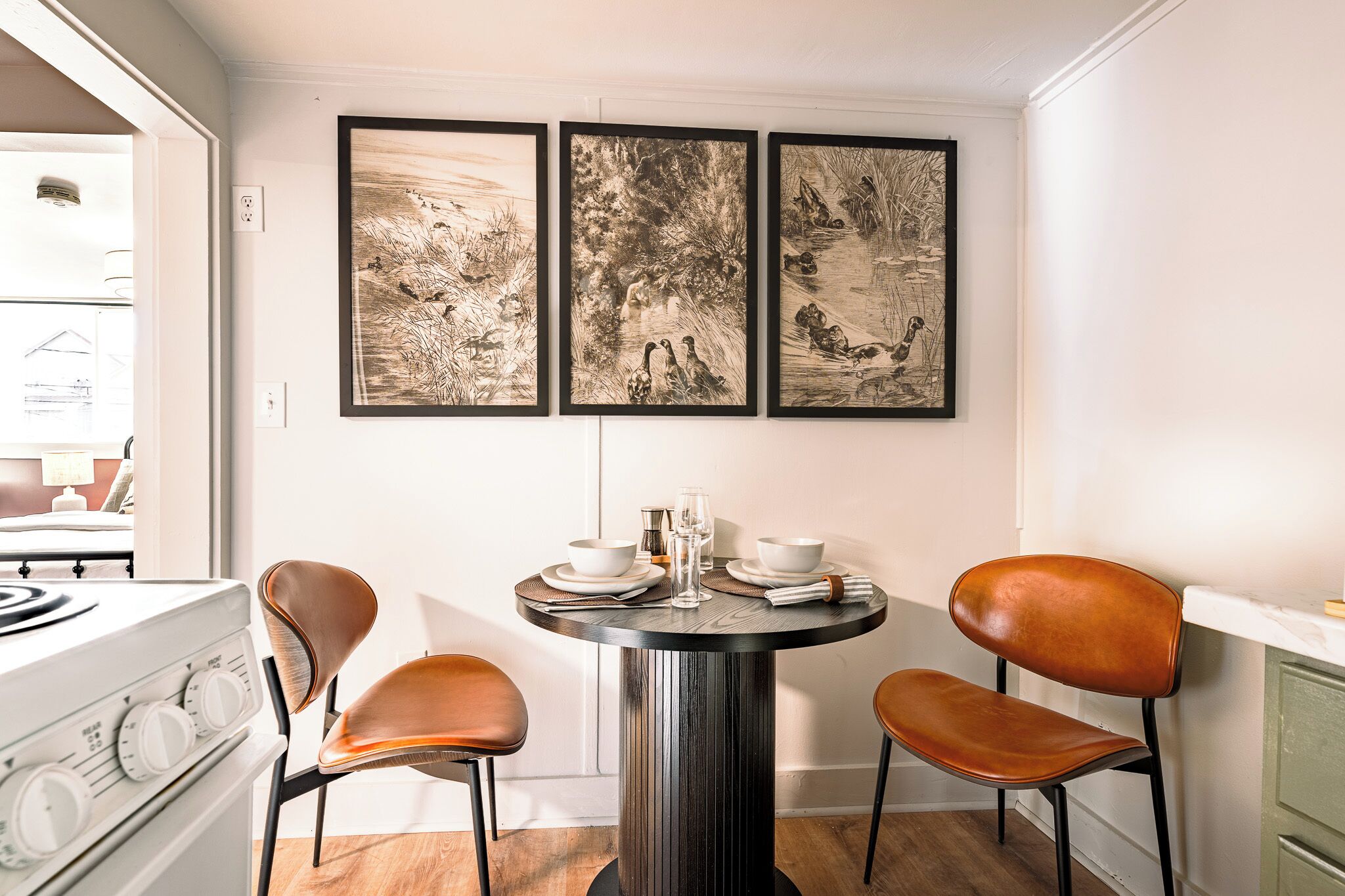 Un coin repas avec une table ronde, deux chaises et trois œuvres d’art encadrées accrochées au mur.