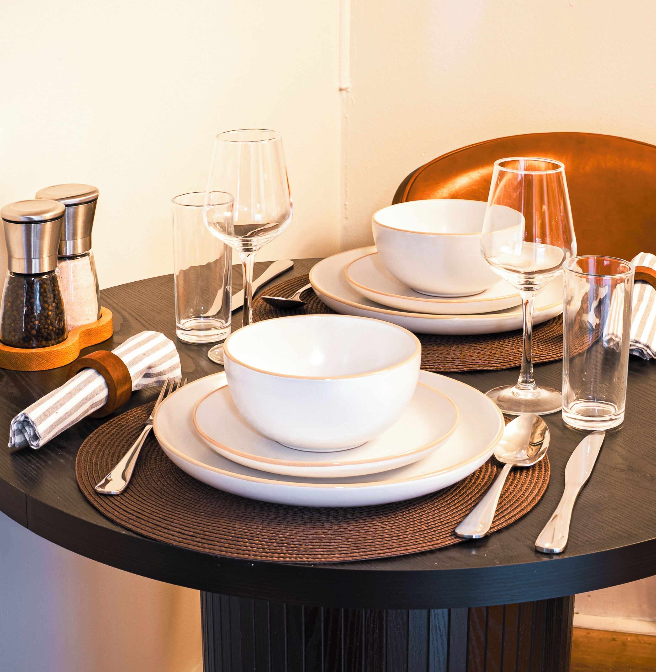 A table set with white bowls, plates, and cutlery, along with two glasses and a bottle.