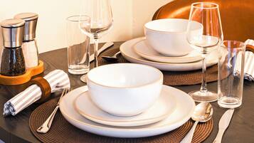 A table set with white bowls, plates, and cutlery, along with two glasses and a bottle.
