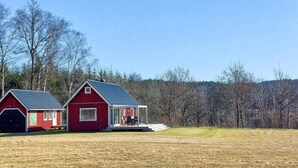 A red barn with a covered porch and a smaller adjacent building, set in a grassy field with trees in the background. - Amazing home in Slättåkra (Slättåkra)