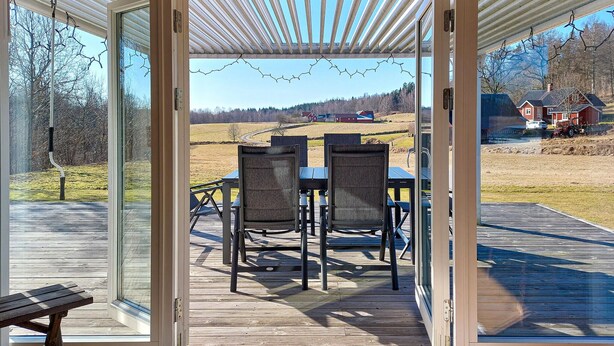 A covered outdoor seating area with a table and chairs, a wooden deck, and a view of a rural landscape. - Amazing home in Slättåkra (Slättåkra)