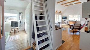 A staircase with a white interior and a wooden ceiling, leading to a living area with a TV, dining table, and chairs. - Amazing home in Slättåkra (Slättåkra)