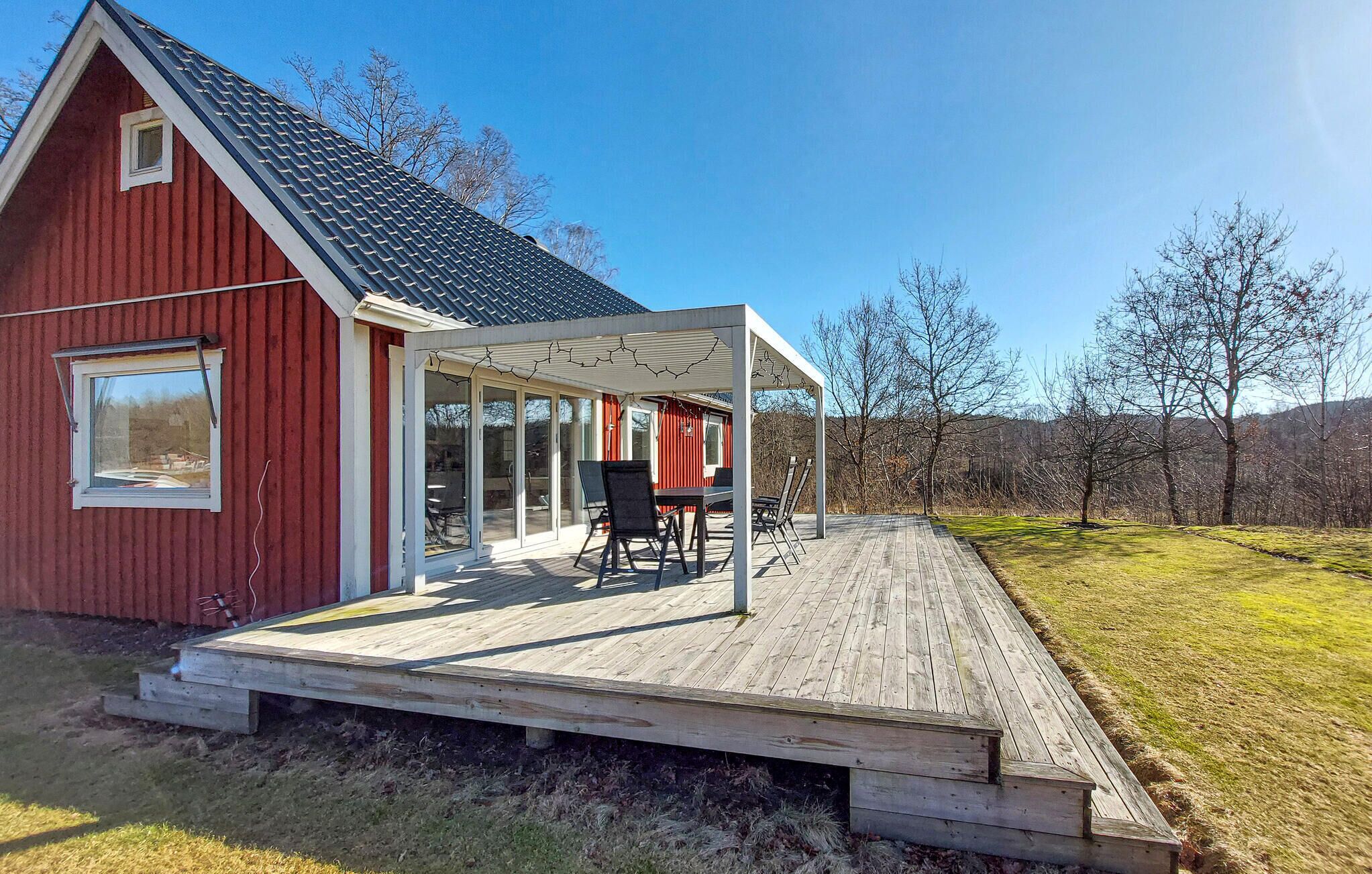 Un bâtiment rouge doté d’un patio couvert, d’une table avec des chaises et d’une terrasse en bois.