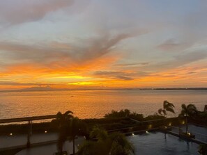 Une vue sur un coucher de soleil au-dessus d’une étendue d’eau, avec un pont et des palmiers au premier plan.