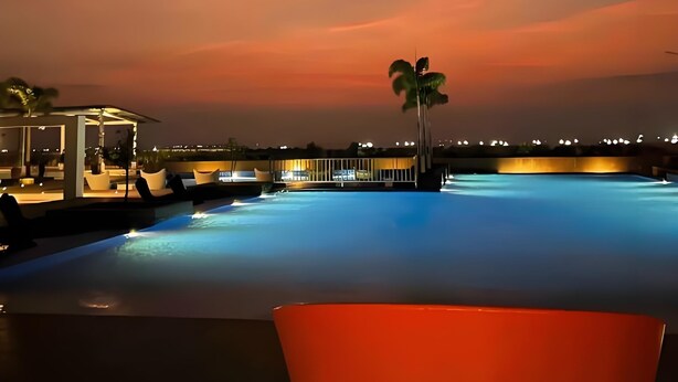 Una piscina con vista sul tramonto, una palma e un'area relax con sedie.