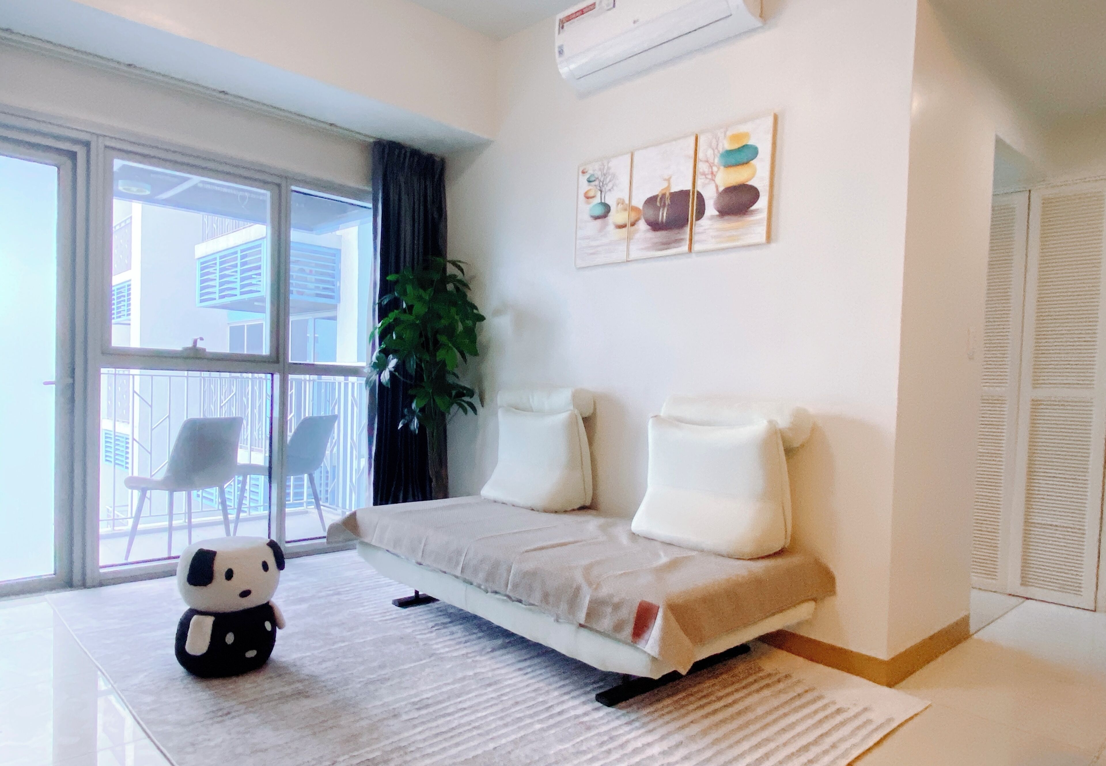 Una sala de estar moderna con un sofá, un peluche de panda, un ventanal grande y una planta.
