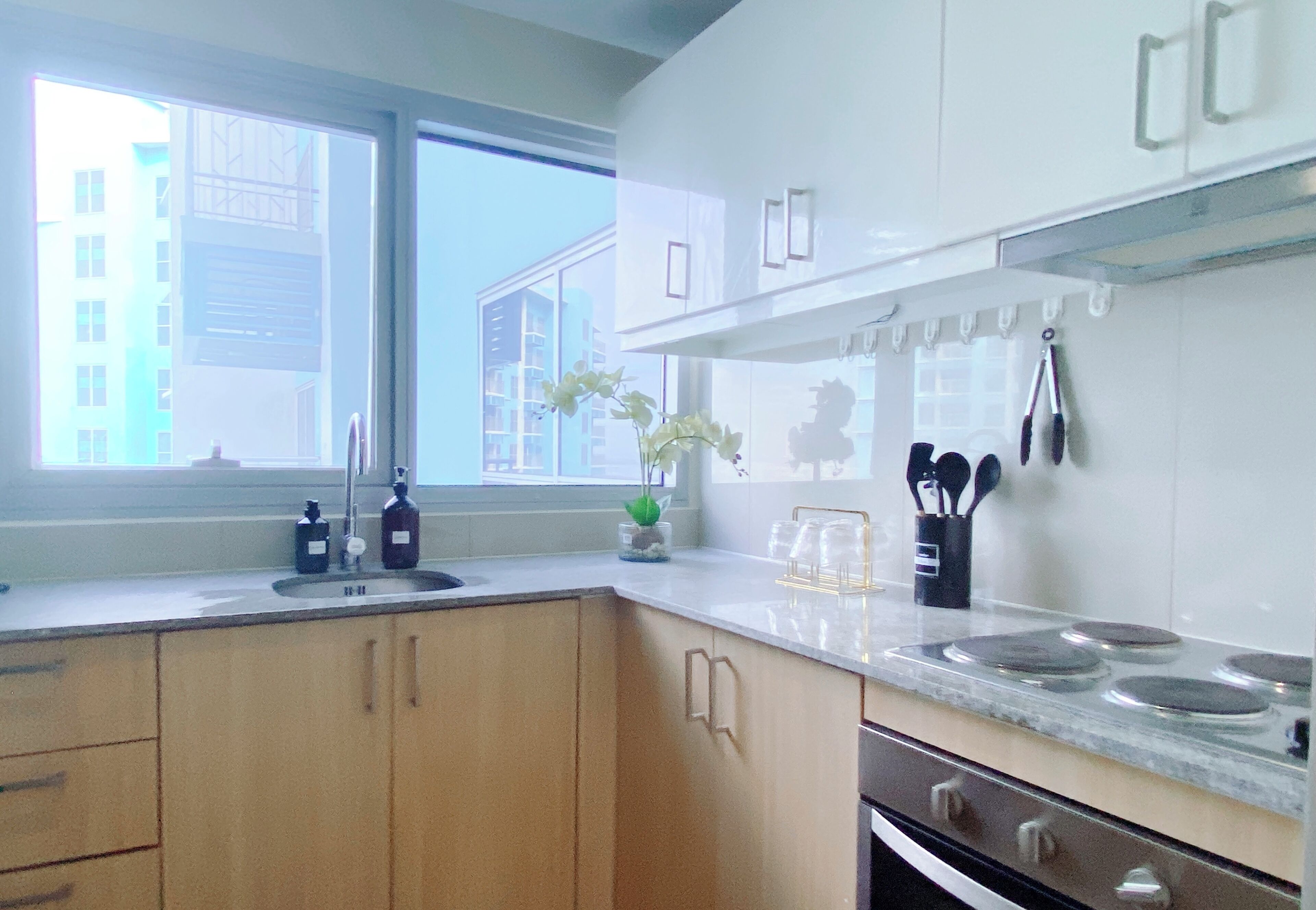 A modern kitchen with wooden cabinets, a stainless steel sink, and a window providing a view of buildings outside.