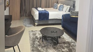 Un dormitorio moderno con cama, sofá, sillón, una mesita de centro y una lámpara en el techo.