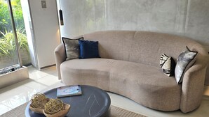Una sala de estar moderna con un sofá beige, una mesa de centro redonda con adornos, y un ventanal con vistas a zonas verdes.