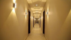 A long, narrow hotel hallway with light fixtures on the walls and a tiled floor. - Hotel Eastleigh (Ludhiana)