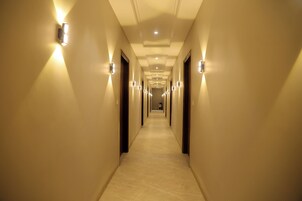 Un pasillo largo y estrecho en un hotel, con lámparas en las paredes y suelo de baldosas.