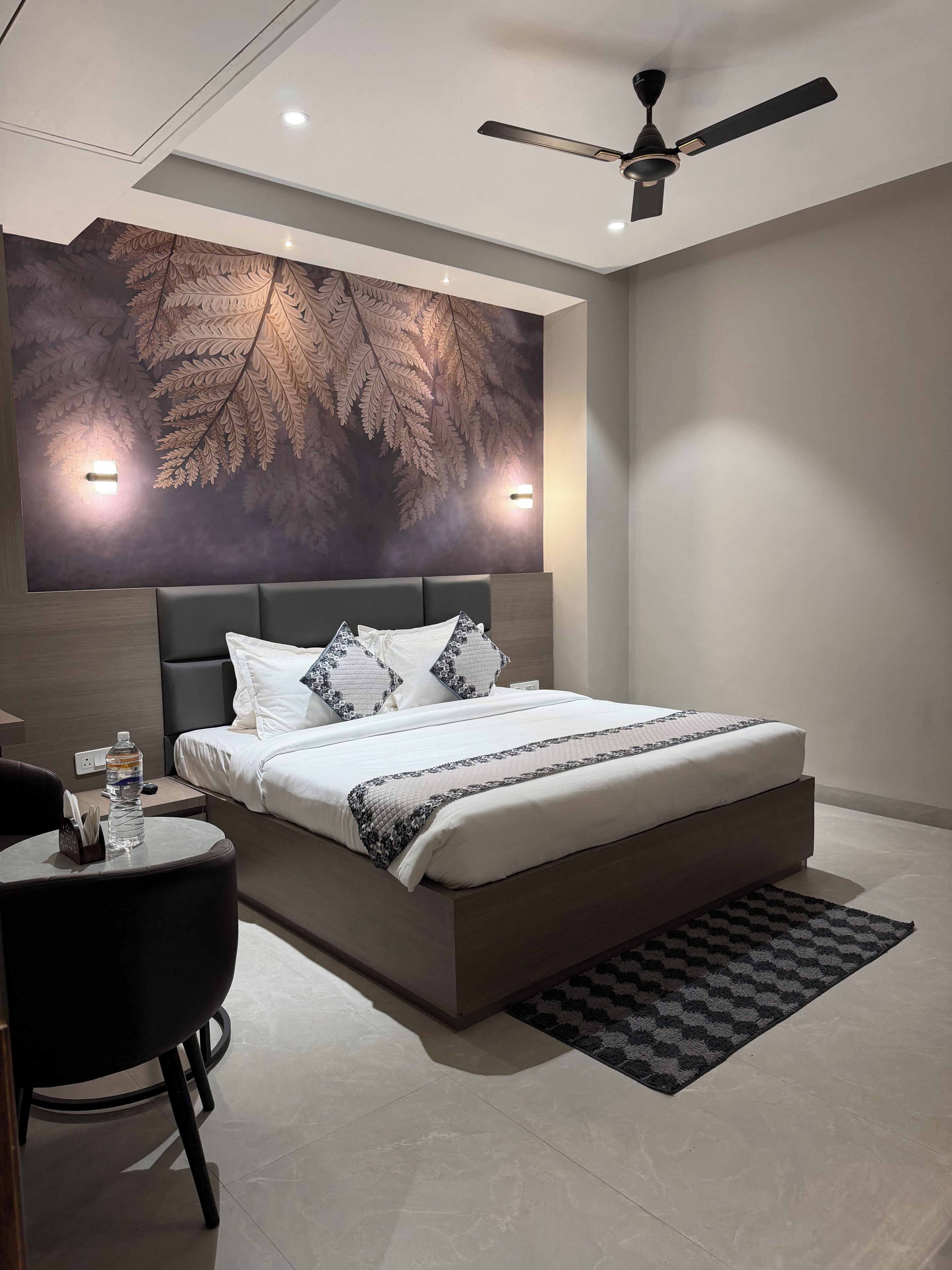 Une chambre à coucher moderne avec un grand lit, un ventilateur de plafond et un luminaire fixé au mur.