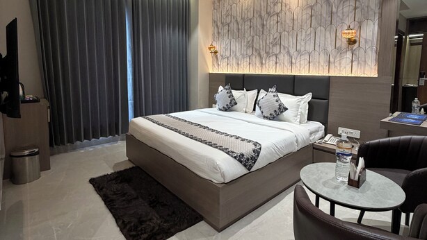 A modern bedroom with a large bed, a ceiling fan, a marble-patterned wall, a small round table, and a dark leather chair. - Hotel Eastleigh (Ludhiana)