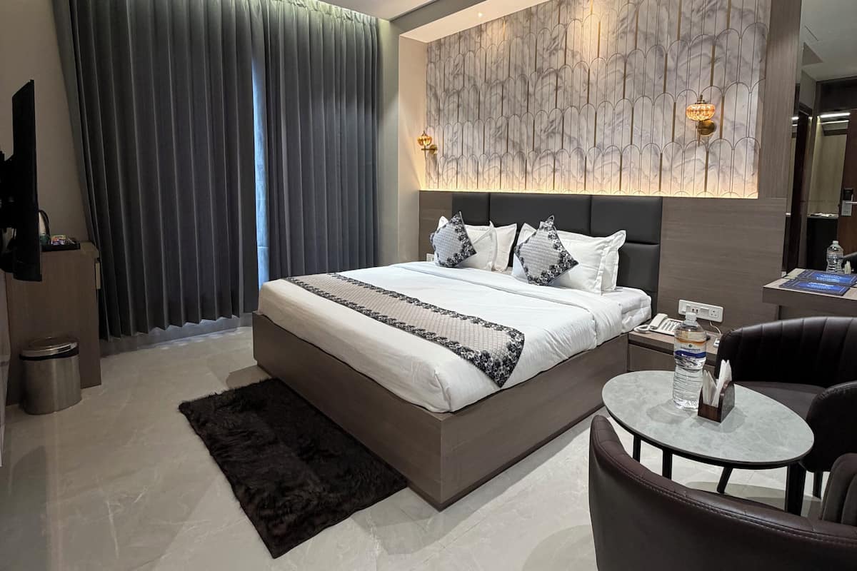 A modern bedroom with a large bed, a ceiling fan, a marble-patterned wall, a small round table, and a dark leather chair.