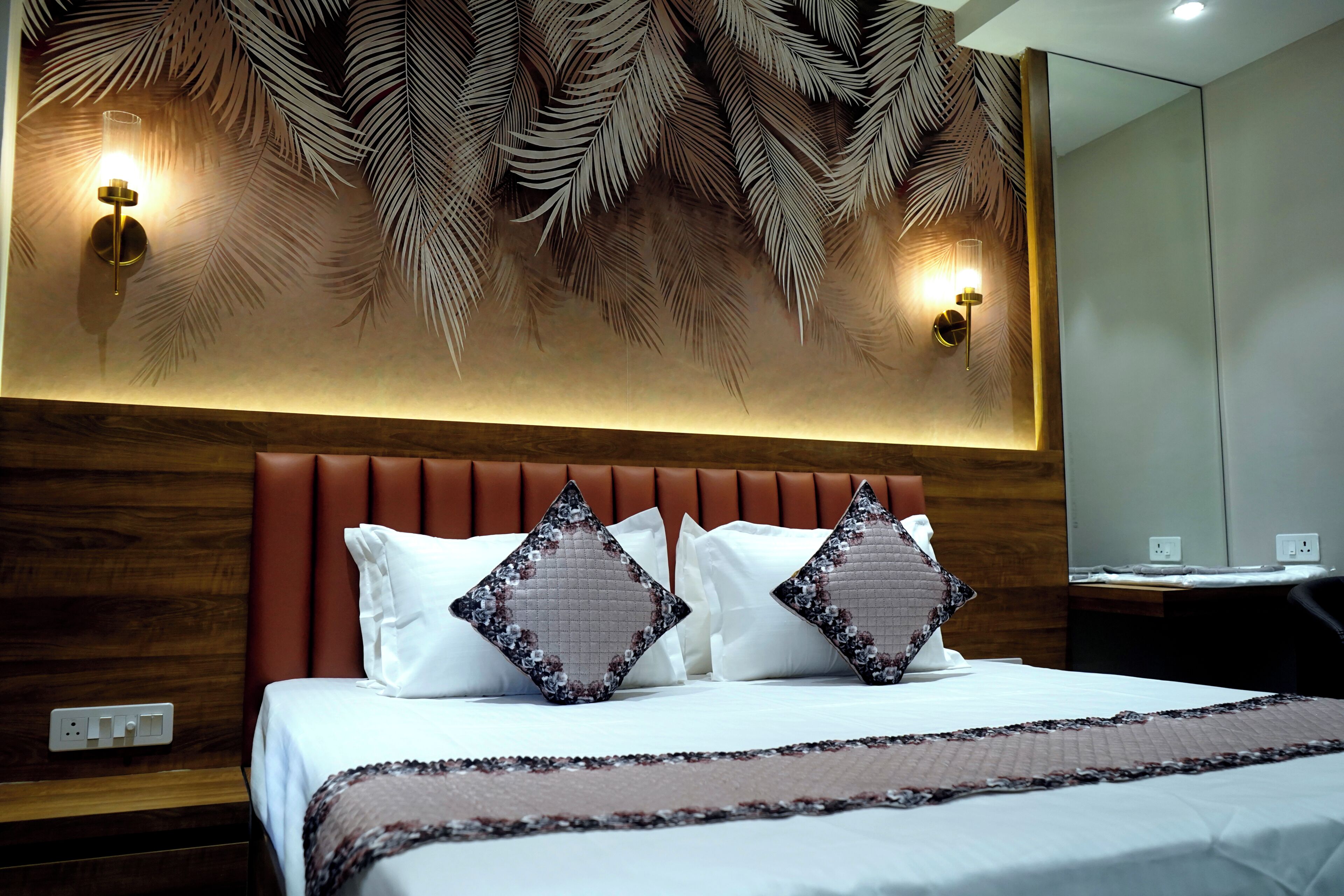 Une chambre d’hôtel avec un lit, une tête de lit, des lampes fixées au mur et un motif décoratif en forme de feuilles sur le mur.