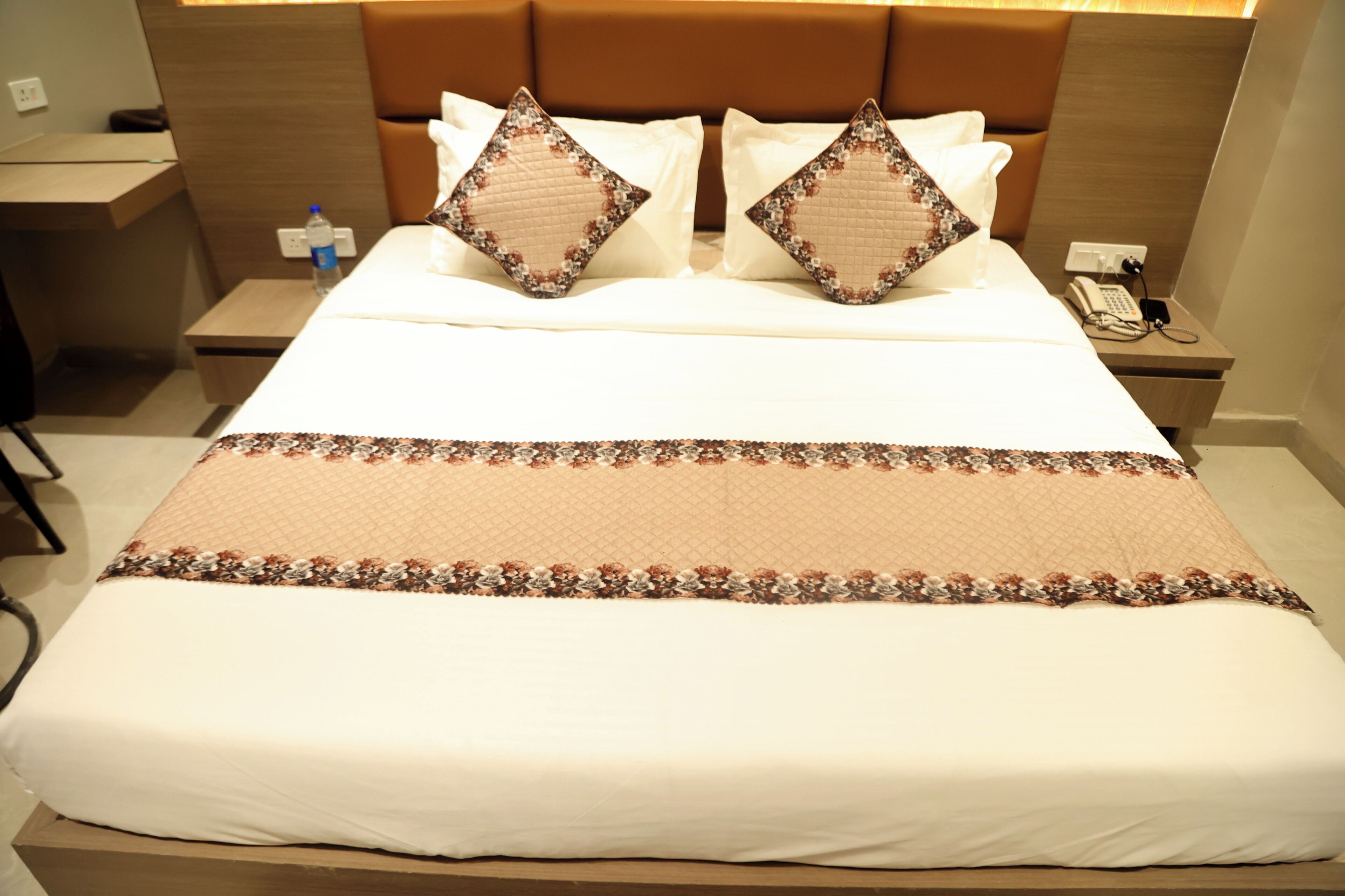 A hotel room with a bed, two nightstands, a telephone, and a water bottle.