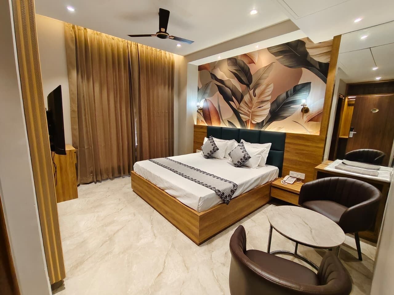 Une chambre d’hôtel moderne équipée d’un lit, d’un bureau, d’une chaise, d’un ventilateur de plafond et d’une grande fresque murale.