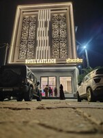 Fachada moderna de un hotel, con señalización iluminada y zona de estacionamiento visible.